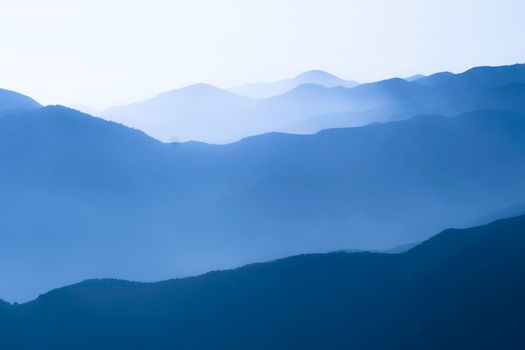 Scenic view of blue mountain ranges enveloped in a misty fog, creating a tranquil landscape.