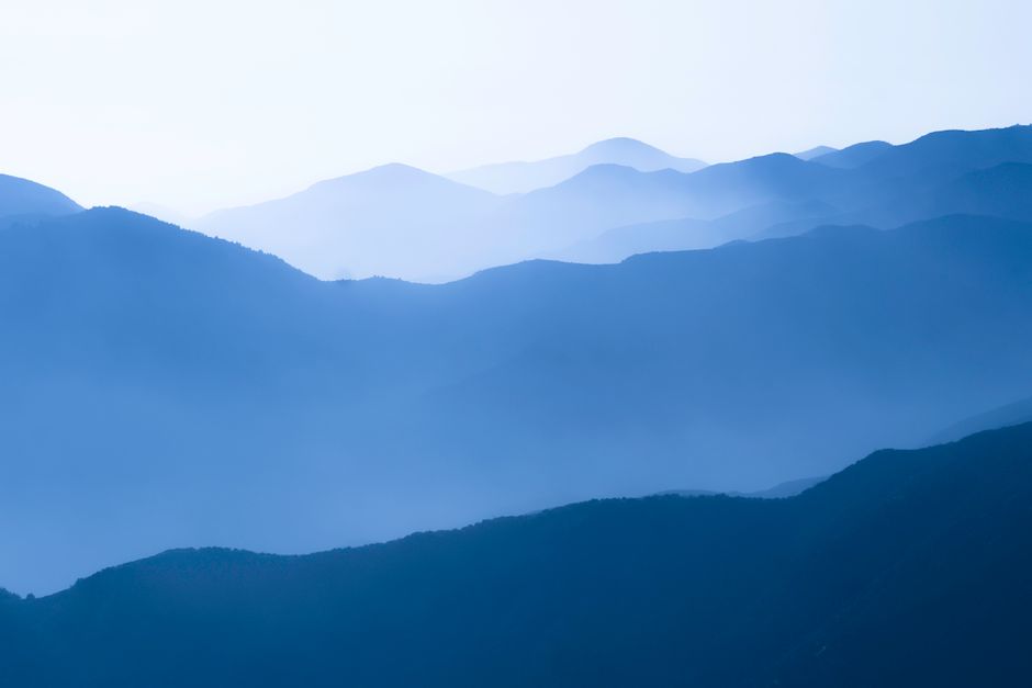 Scenic view of blue mountain ranges enveloped in a misty fog, creating a tranquil landscape.