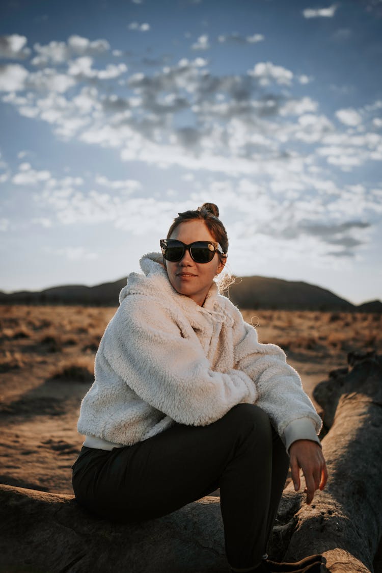 Woman In White Faux Fur Jacket And Black Leggings Sitting In Steppe On Sunny Day