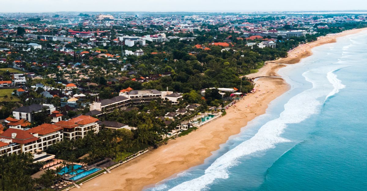 A stunning aerial view of Bali's coastline with waves meeting the sandy shore and green landscapes.