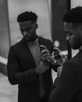 Black and white portrait of a man holding perfume in front of a mirror.