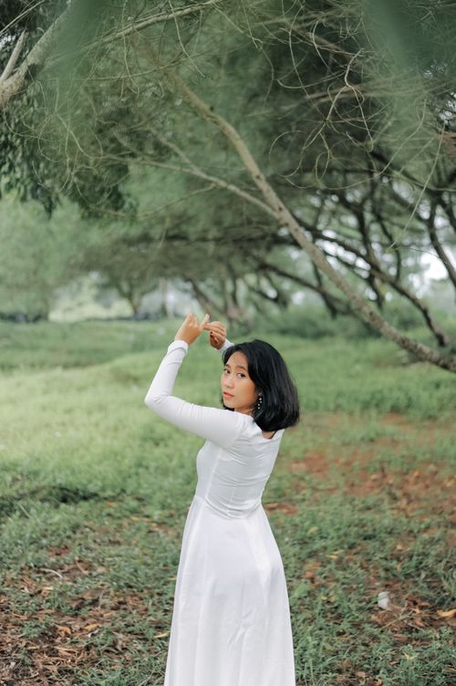Free A woman in a white dress posing elegantly in a lush, green forest setting during the day. Stock Photo