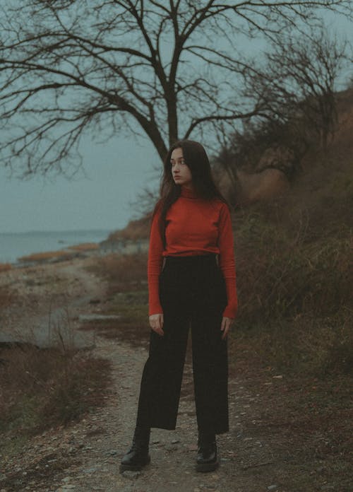 A Woman in Red Turtleneck Sweater and Black Pants Standing on a Dirt Ground