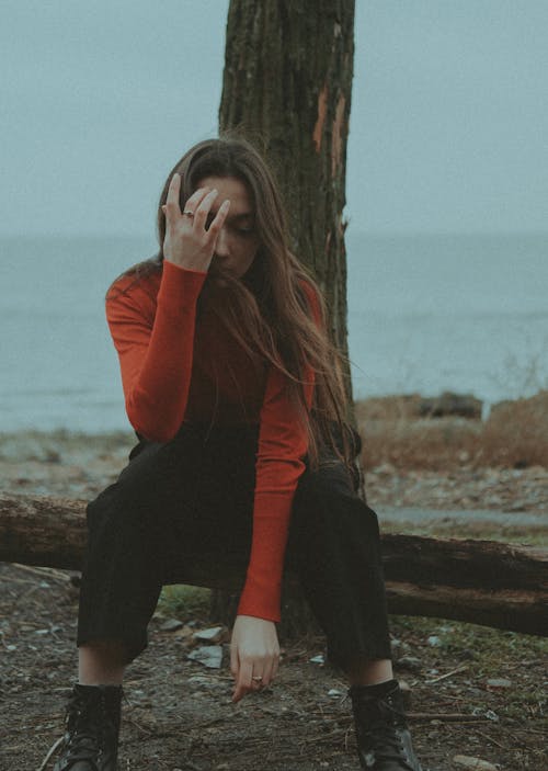 Free A Woman in Red Sweater and Black Pants Sitting on a Tree Trunk Stock Photo