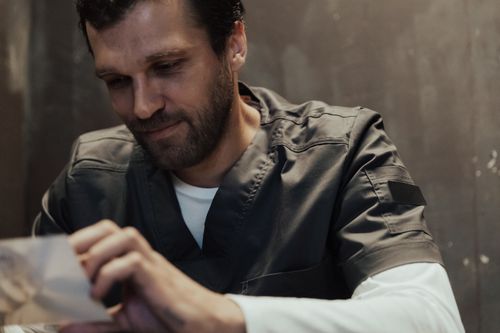 Free A man in scrubs smiles quietly while looking at an object indoors, conveying introspection. Stock Photo