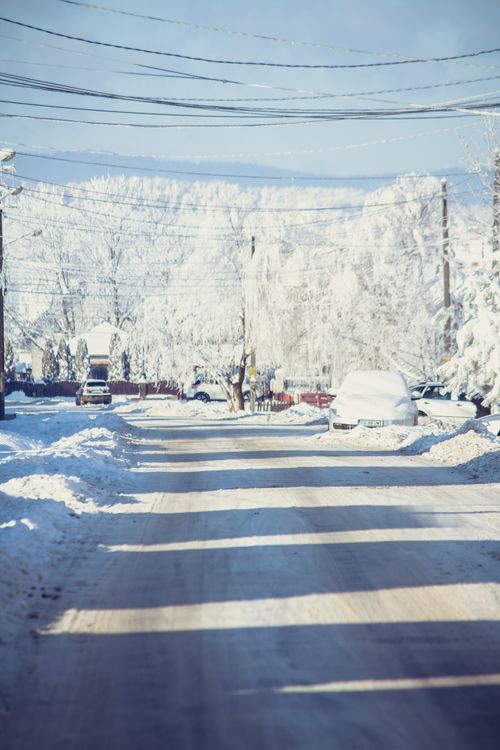 Free Serene winter street blanketed in snow with parked cars and clear blue sky. Stock Photo