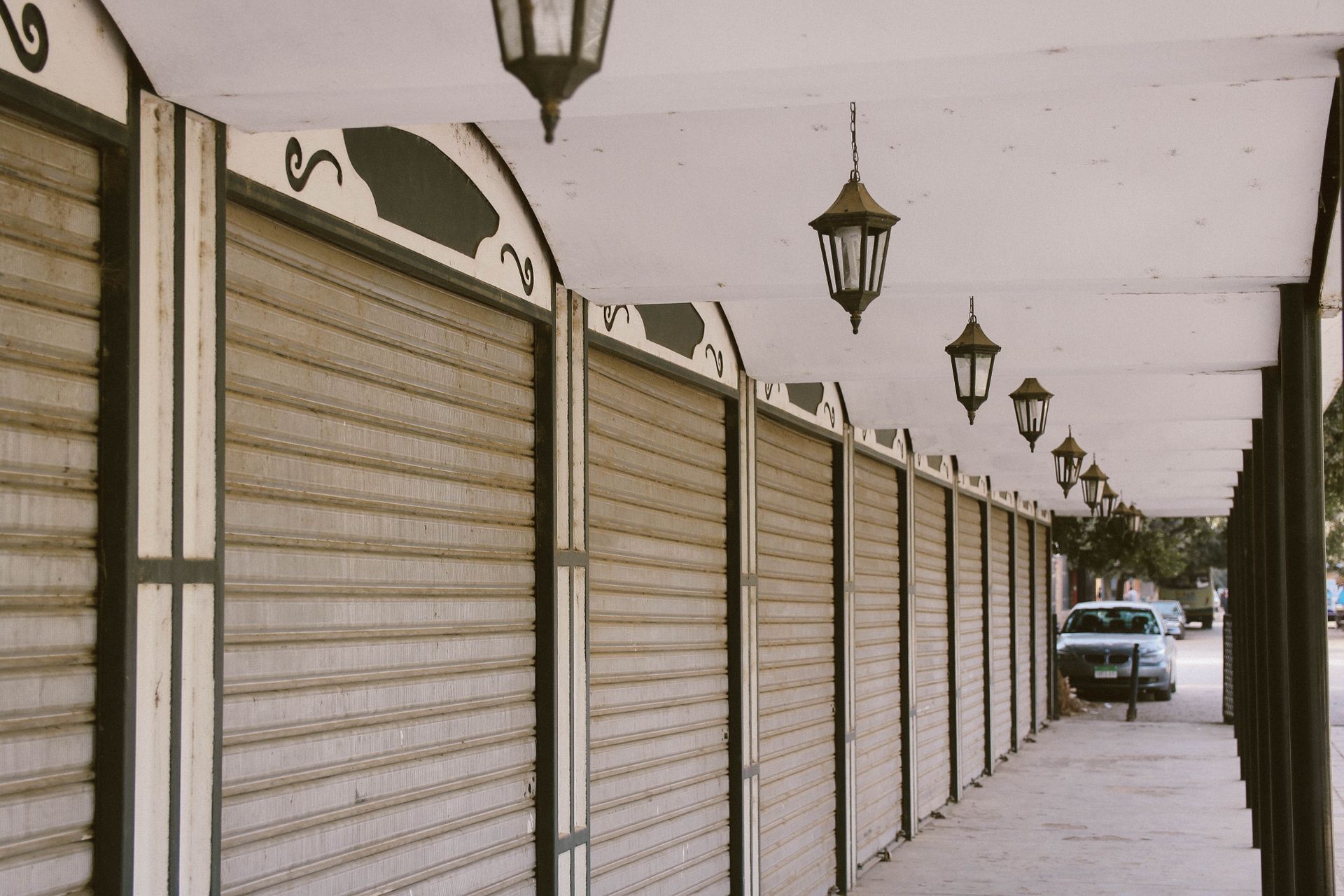 A quiet urban street featuring closed storefronts with decorative lanterns.