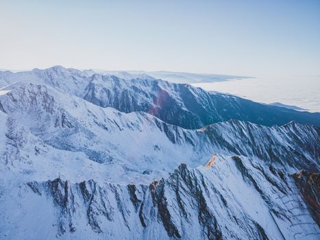 Aerial view of the majestic snow-capped Carpathian Mountains in Romania under a clear blue sky.