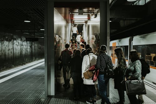 Fotografi Grayscale Orang Yang Berbaris Di Stasiun Kereta