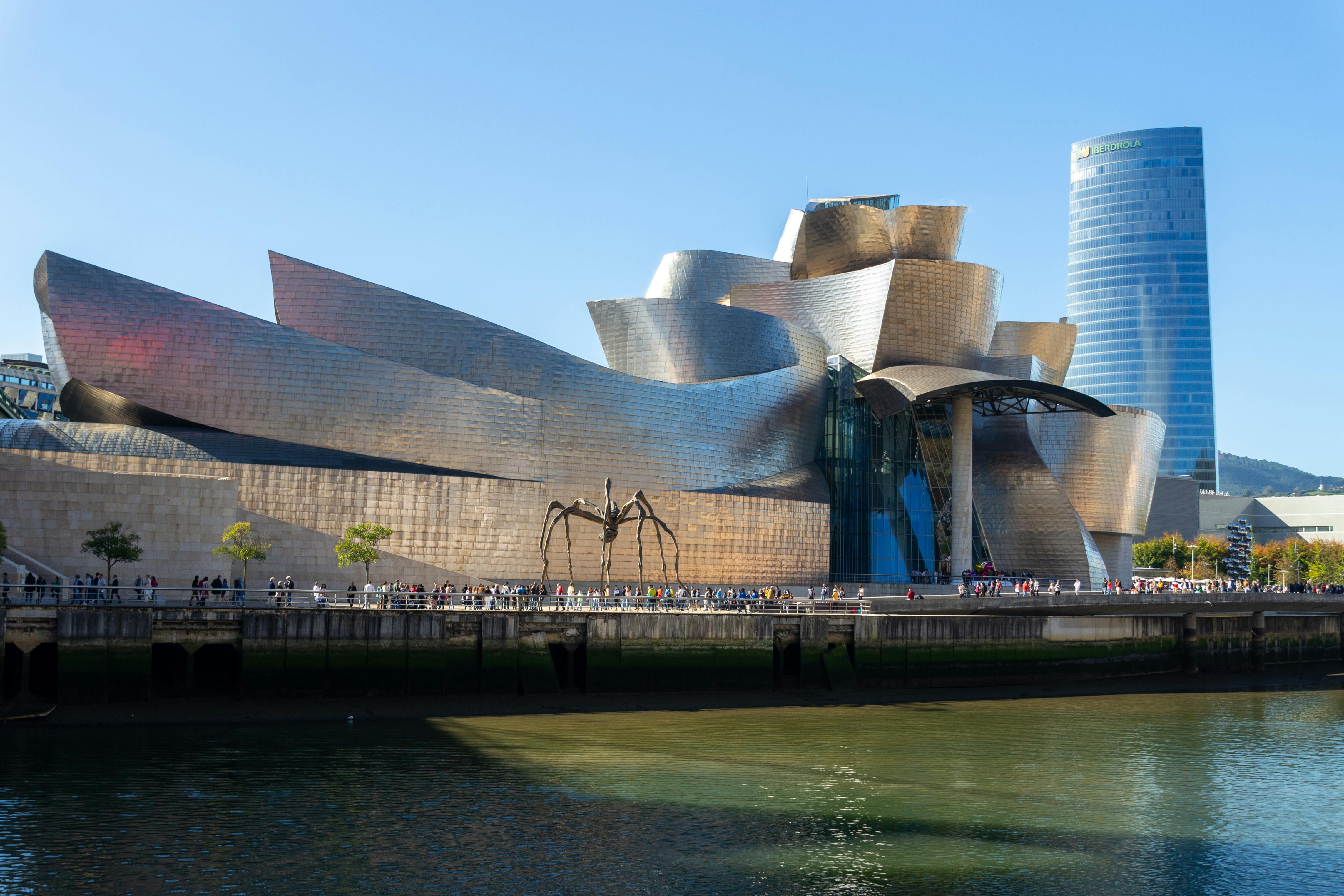The iconic Guggenheim Museum in Bilbao by the river under a clear blue sky. - Bilbao