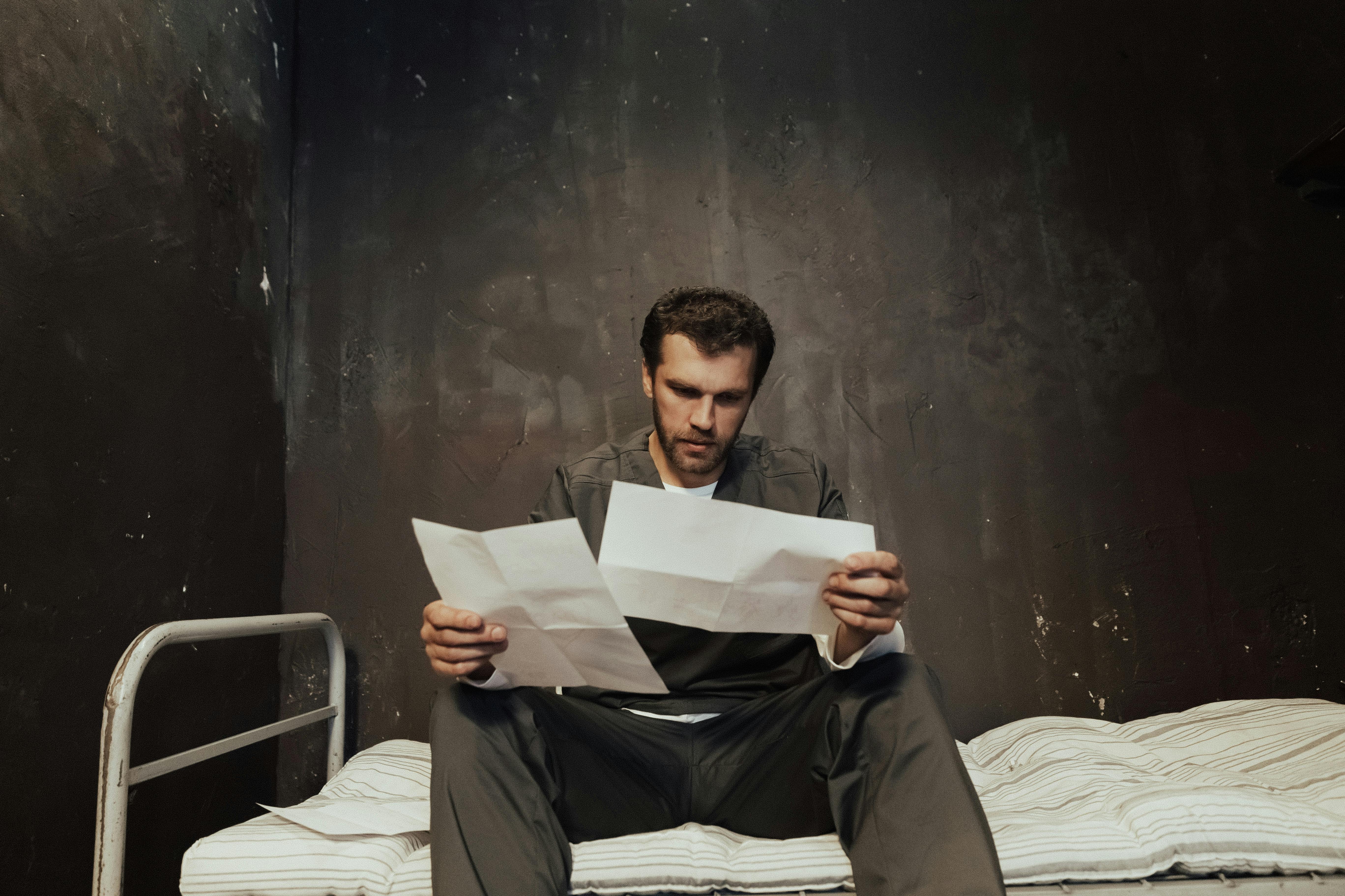 man sitting on bed holding white papers