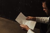 A man sitting indoors, reading a heartfelt handwritten letter.