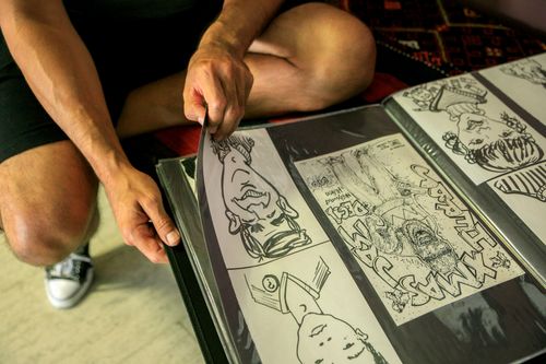 Free A person wearing shorts and sneakers turning pages of a comic art album, with close-up on hands and drawings. Stock Photo