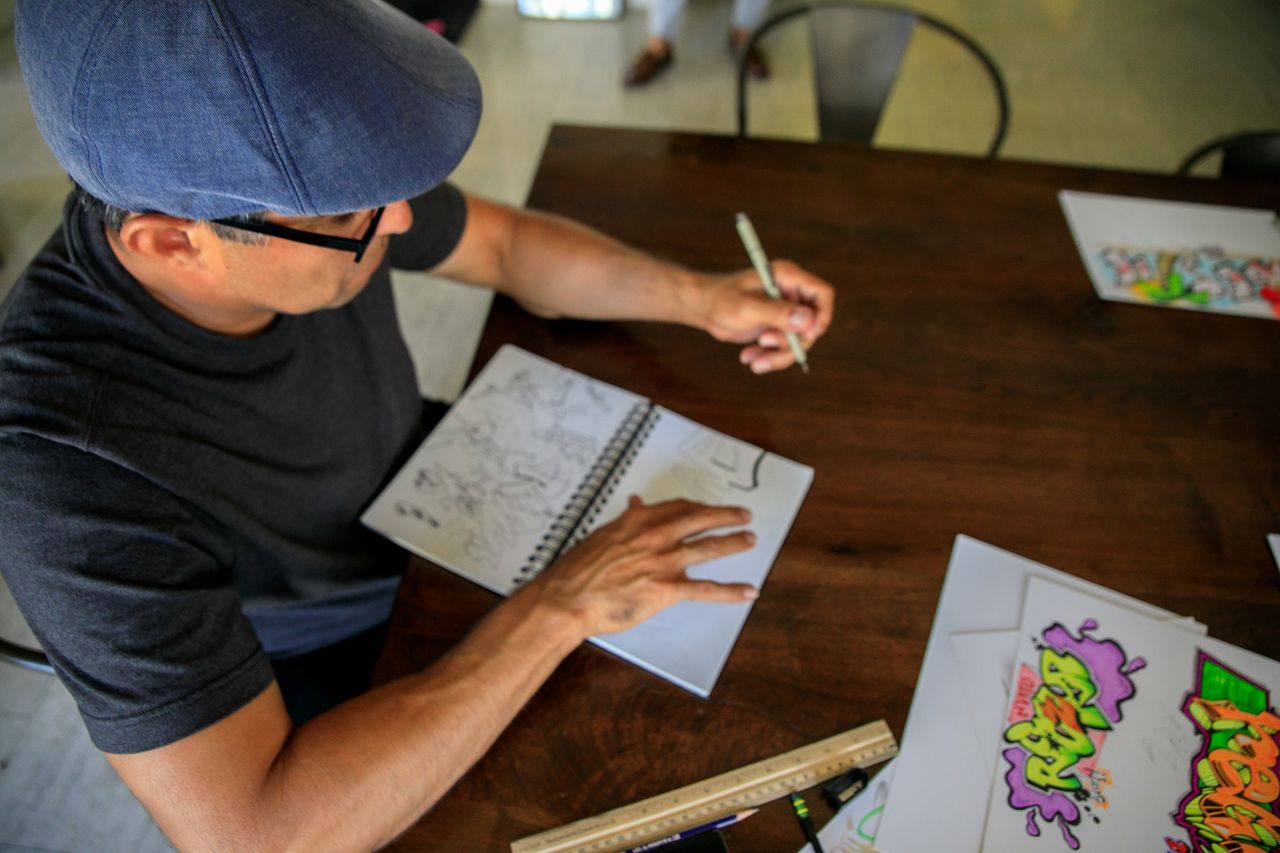 top view of a man sketching graffiti art in a notebook at a wooden des