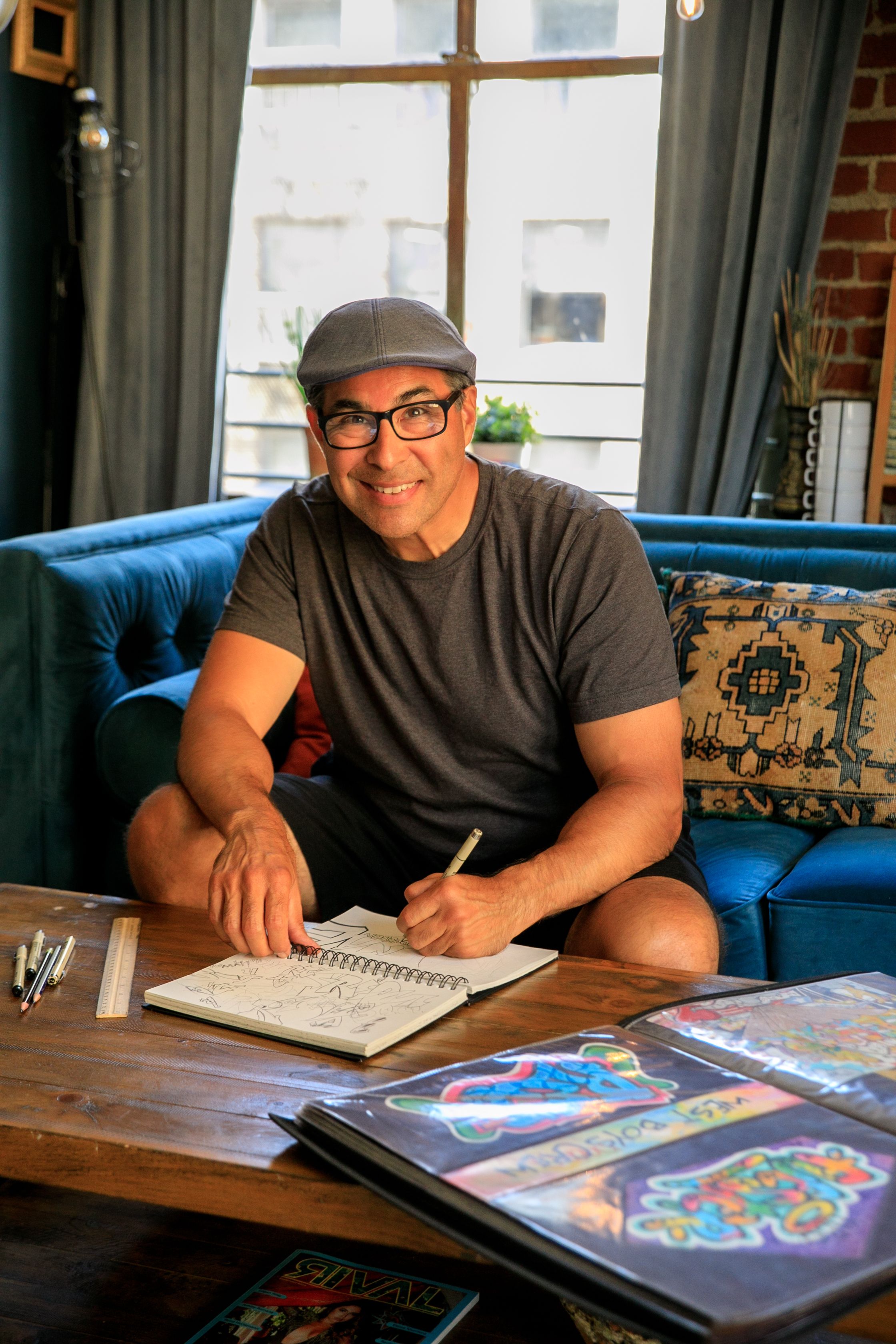 Smiling man drawing in sketchbook with art tools in a cozy studio setting.
