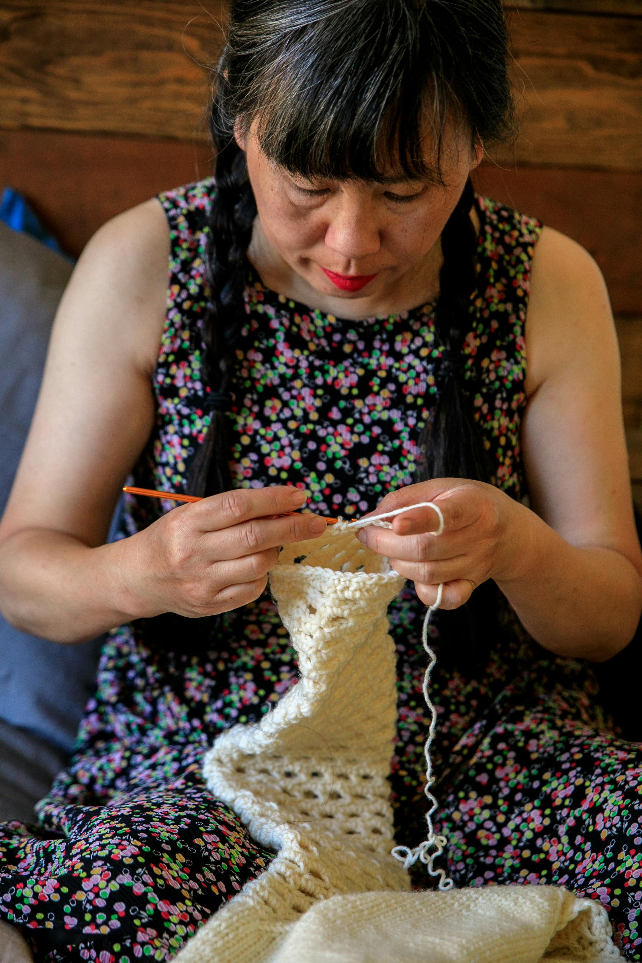 Woman seated indoors, deeply focused on knitting with white yarn. Captures a serene crafting moment.