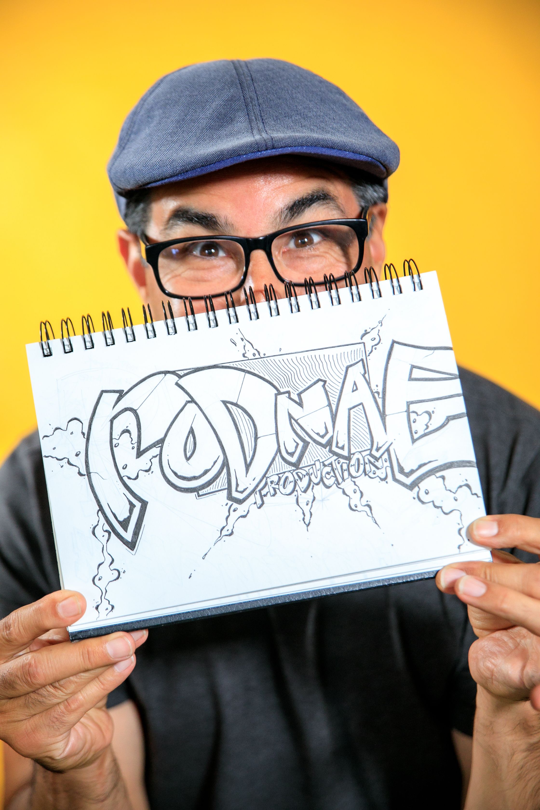 Man presenting a unique black and white drawing in a sketchbook against a vibrant yellow background.