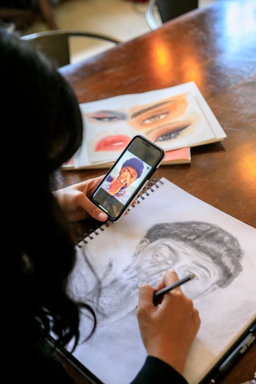 Free A woman using a smartphone to create a detailed pencil portrait on paper. Stock Photo