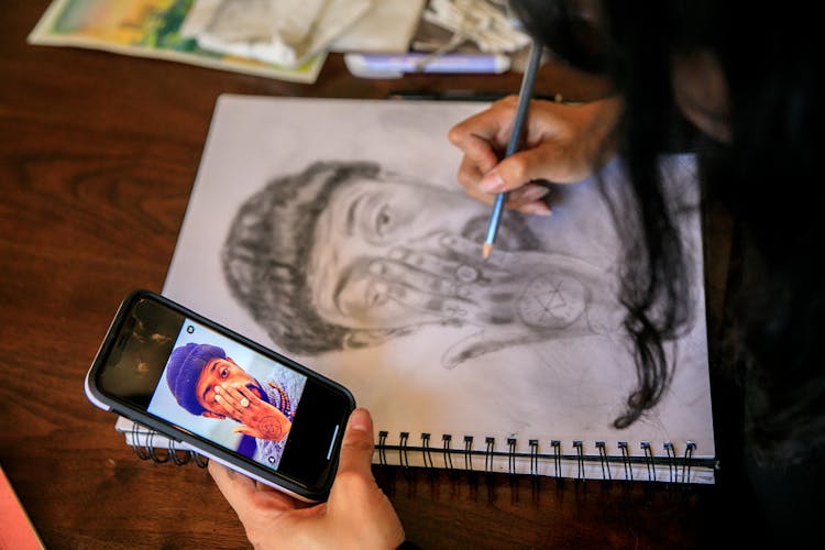 Artist Drawing Male Face In Spiral Notebook From Picture In Her Smart Phone