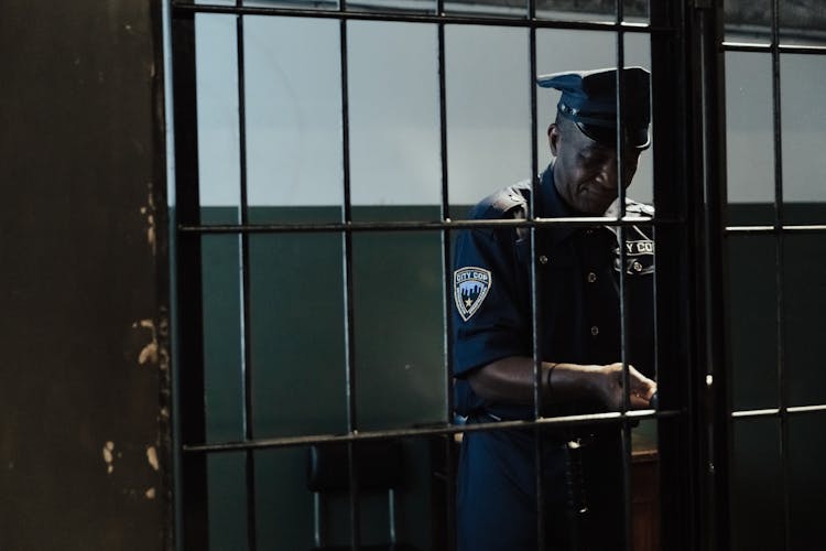 Man In Blue Uniform Standing Beside Black Bars