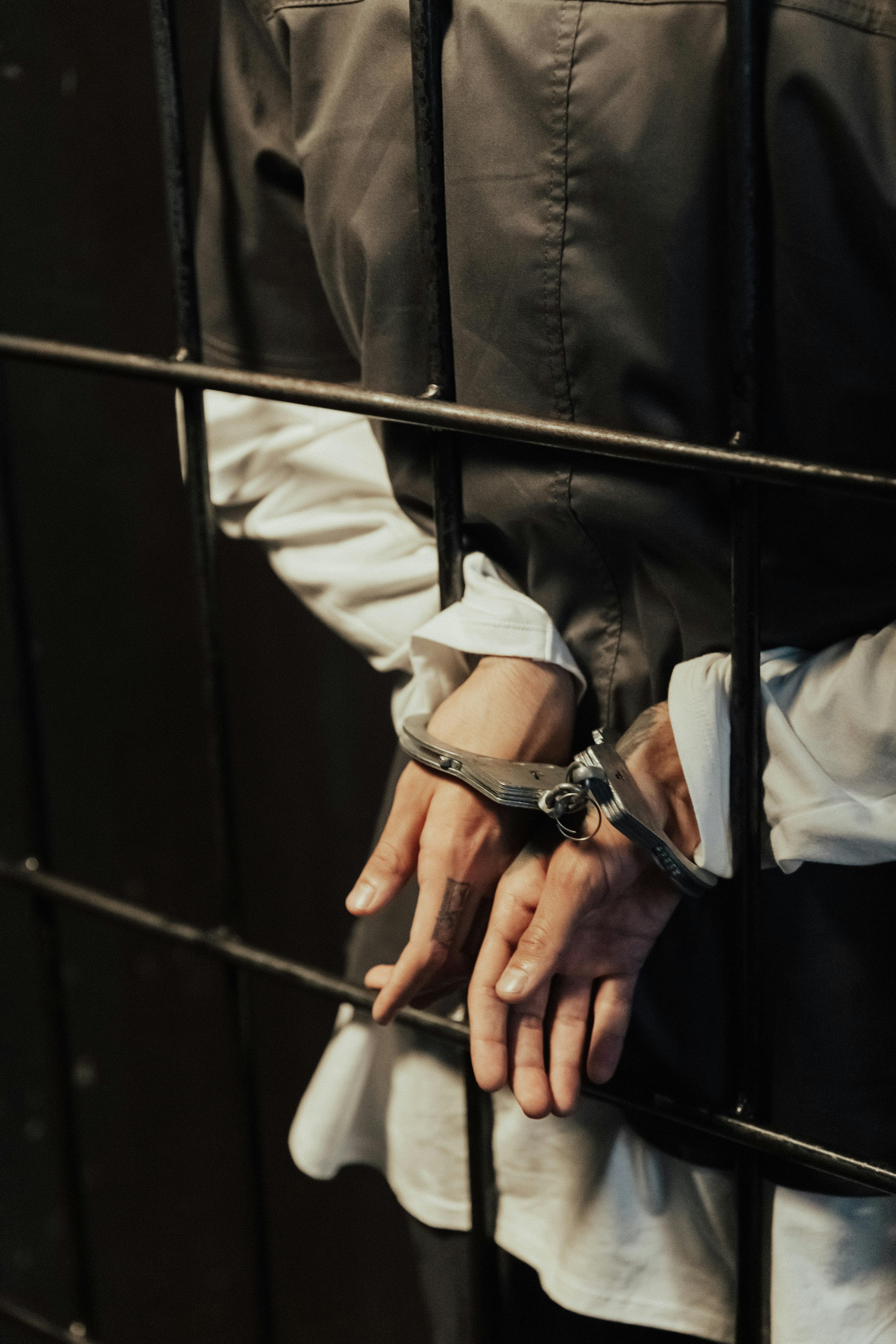 hands of a person in handcuffs near metal bars