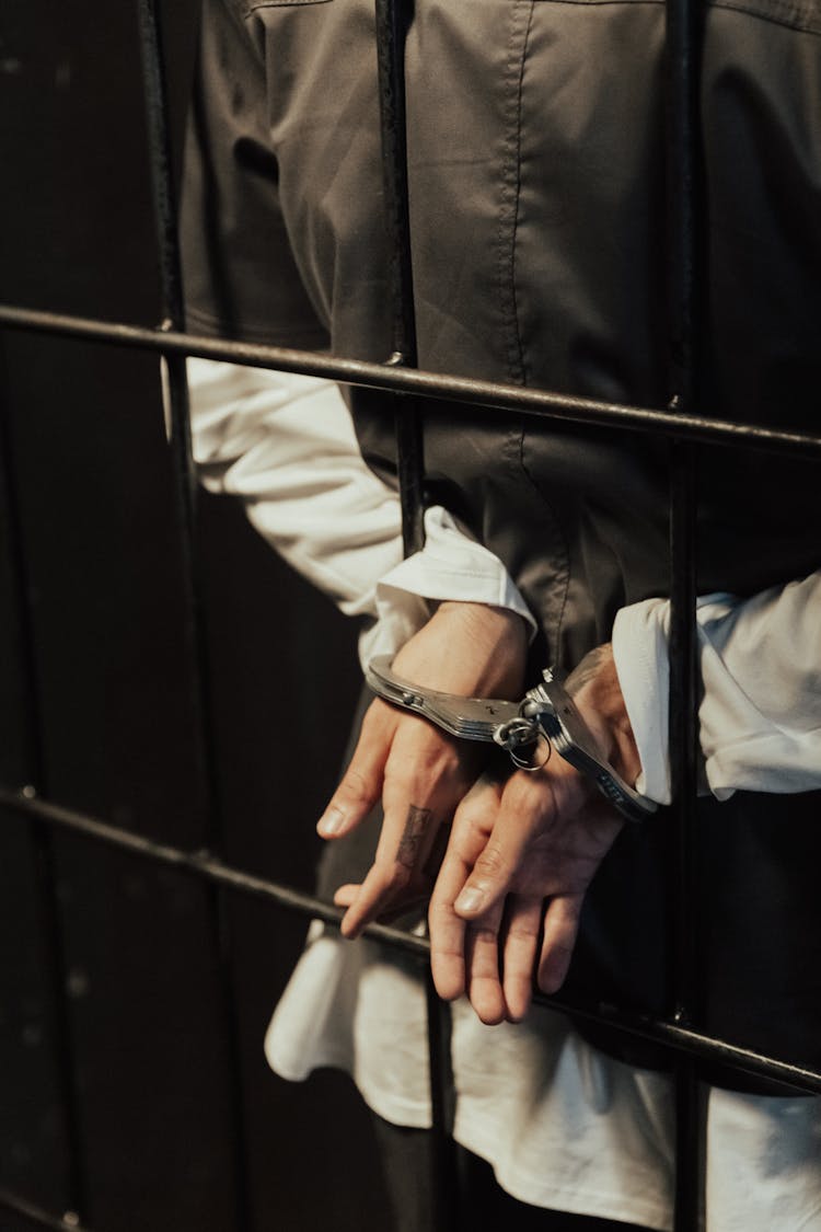 Hands Of A Person In Handcuffs Near Metal Bars