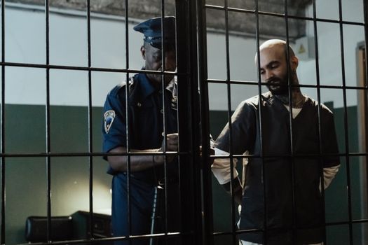 A policeman arrests a bald man in a dimly lit prison cell, conveying confinement.