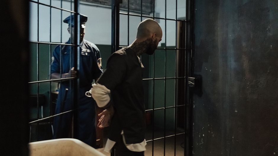 Police officer escorting a handcuffed prisoner through a dimly lit jail corridor.