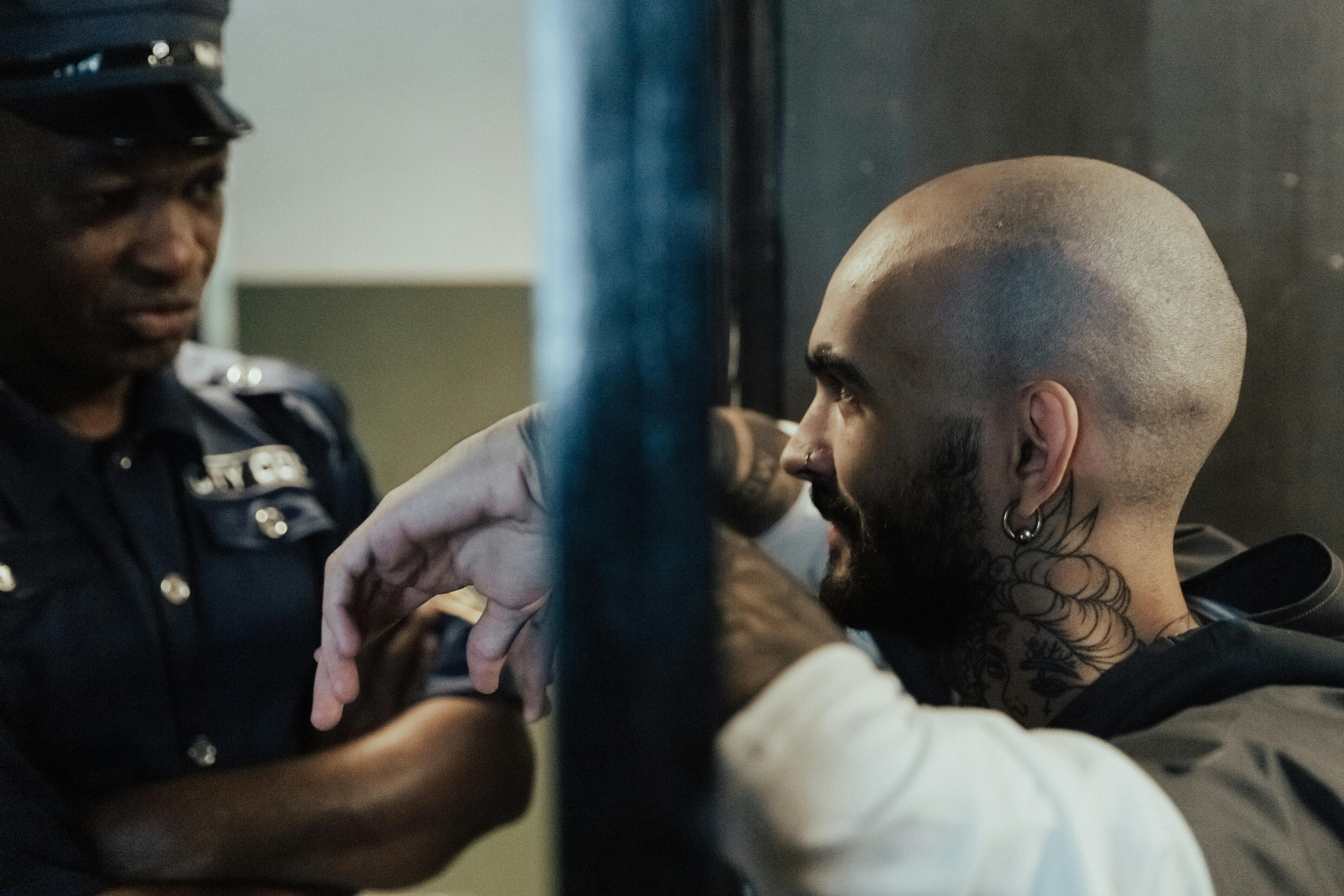 Bald Man with Tattoo in Jail Near a Policeman · Free Stock Photo
