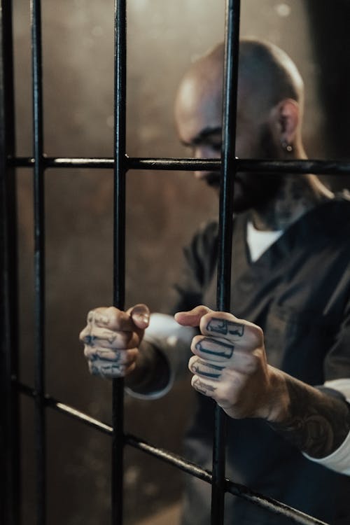 Man in Black and White Long Sleeve Shirt Standing beside Black Metal Bars