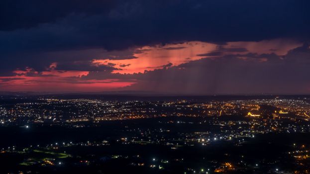 A breathtaking aerial view of a city at night with a dramatic red sky backdrop, illuminated by city lights.