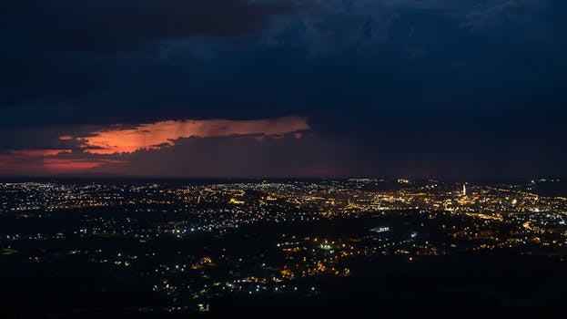 Stunning aerial view of a cityscape at dusk with vibrant city lights and dramatic clouds.