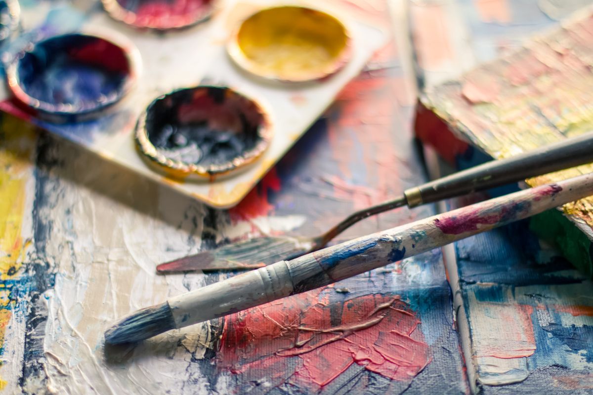 Artist hands mixing acrylic and earth pigments on a wooden palette during an open studio session