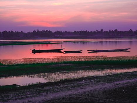 Scenic view of boats silhouetted against a vibrant sunset over a tranquil river.