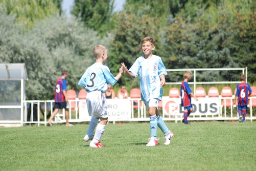 Two young football players in light blue uniforms celebrate a successful play outdoors.