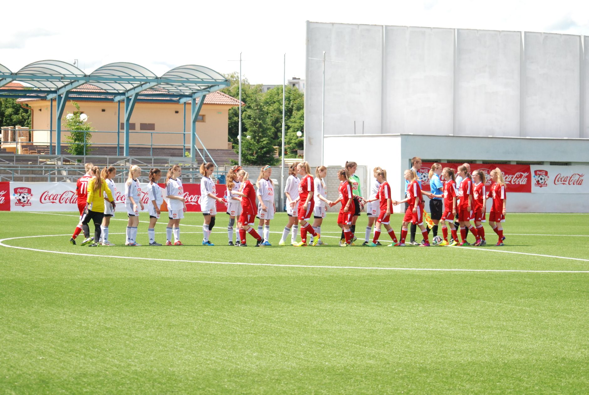 Young women's soccer teams in uniforms shaking hands on the field, promoting sportsmanship.