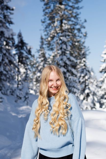 Smiling woman with blond hair in blue sweater in snowy forest.