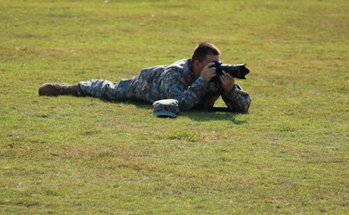 白天使用单反相机在绿色草地上的军事蹲下