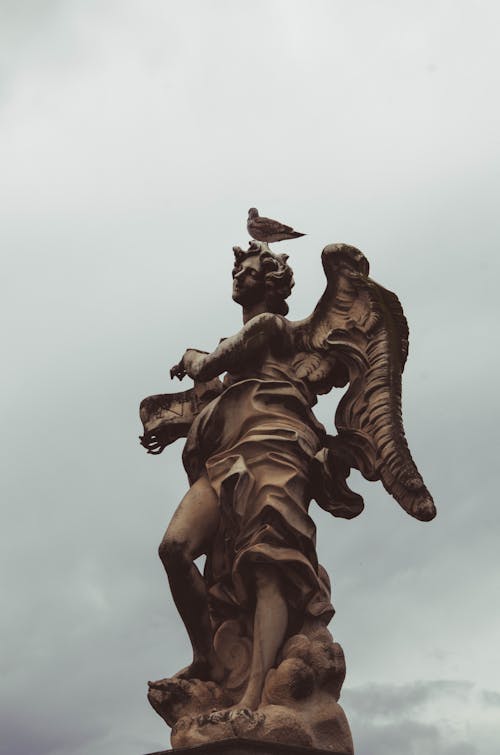 Free Bird Perched on Top of a Statue Stock Photo