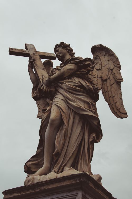 Free A detailed statue of an angel carrying a cross, viewed from below against a cloudy sky. Stock Photo