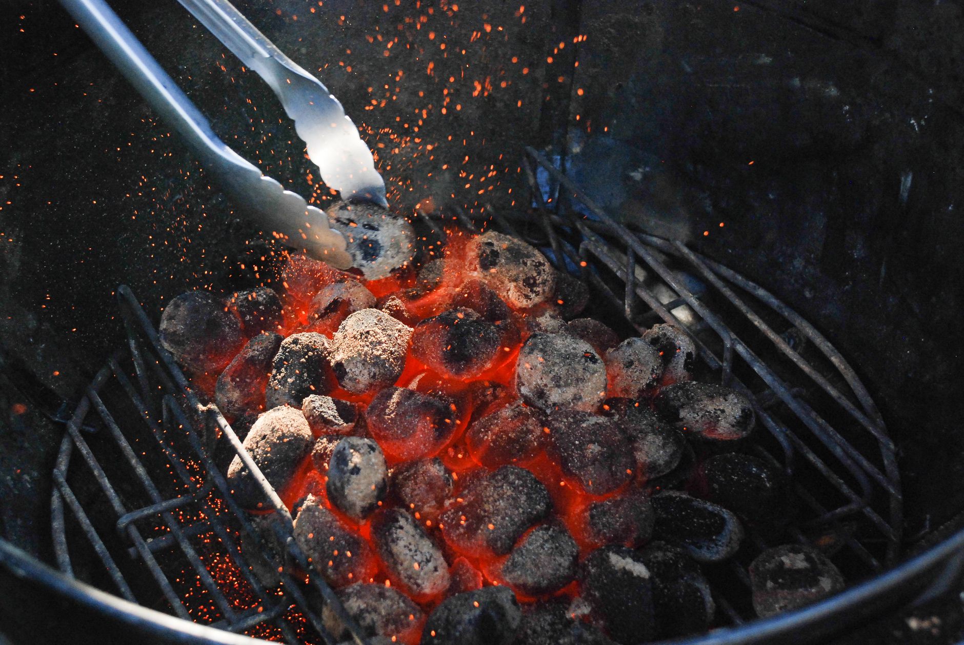 Glowing charcoal and tongs during a low-and-slow kettle setup