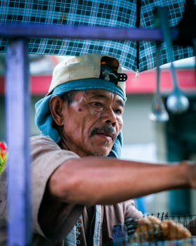 Elderly street vendor selling goods under a colorful umbrella.