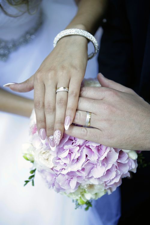 Free Close-up of bride and groom's hands with wedding rings and a bouquet of pink and white flowers. Stock Photo