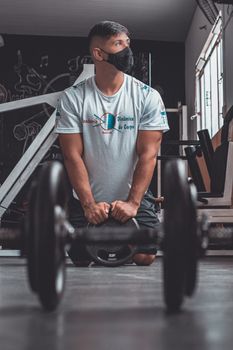 A man wearing a facemask does weightlifting indoors, focusing on fitness and health.