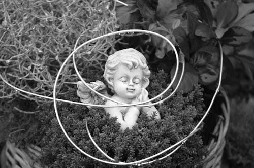 Free Grayscale Photo of an Angel Sculpture Near Green Leaves Stock Photo