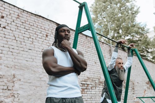 Free Two men exercising on outdoor pull-up bar in urban setting. Stock Photo