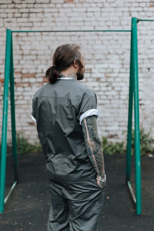 Free A man with tattoos stands outdoors in a prison yard wearing a jumpsuit. Stock Photo