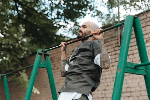 A tattooed man performs exercises on a pull-up bar outdoors, showcasing strength and fitness.