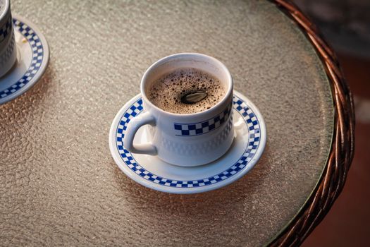 Delightful black coffee served in a blue pattern cup on a glass table outdoors.