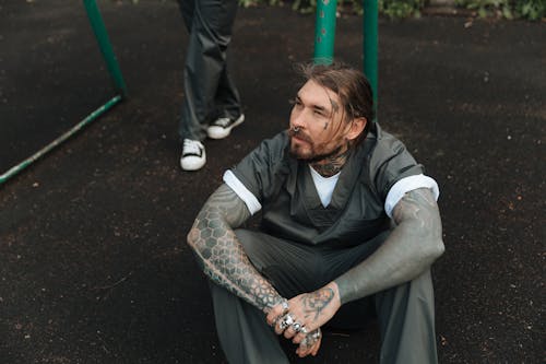 Prisoner with Jewellery and Tattoos sitting in Jail Yard
